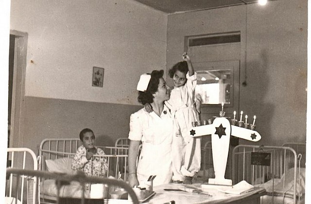 נעמי סמואלוב וילדה ליד חנוכיה בבית החולים לילדים בהנהלת "הדסה" בראש העין, התמונה מאלבום "נעמי ושלמה סמואלוב" באתר "ישראל נגלית לעין"